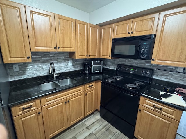 kitchen with a sink, light wood-style floors, dark stone counters, black appliances, and tasteful backsplash