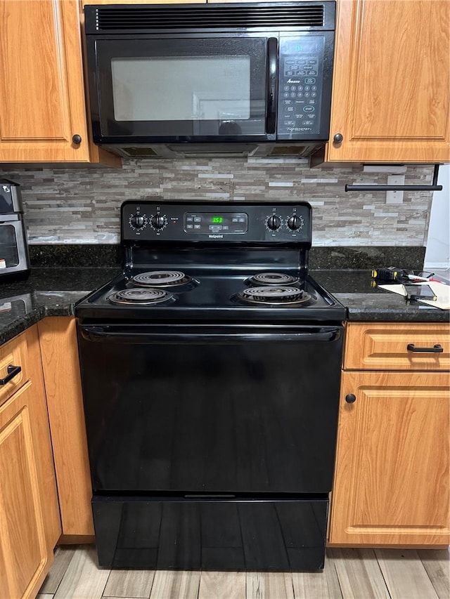 kitchen featuring black appliances, decorative backsplash, and dark stone countertops