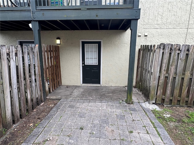 view of exterior entry with fence, a balcony, and stucco siding