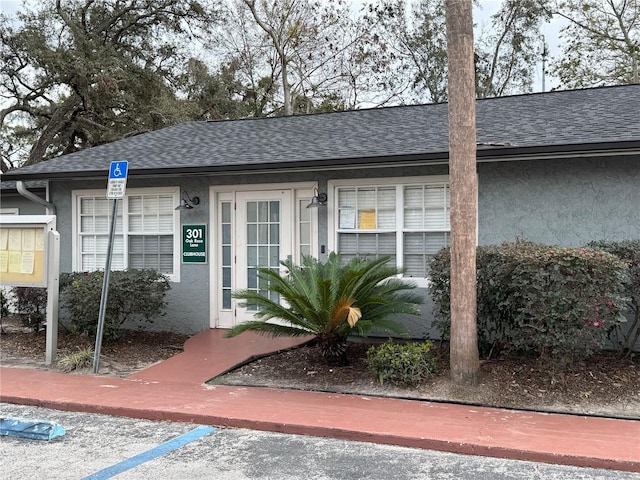 entrance to property featuring roof with shingles and stucco siding