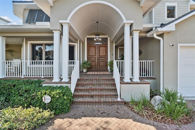 doorway to property with a garage, covered porch, and stucco siding
