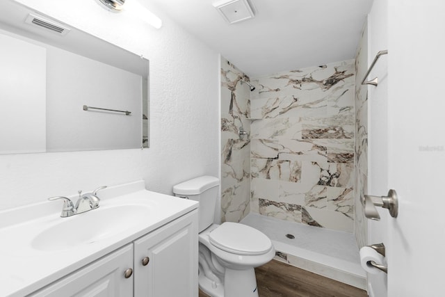 bathroom featuring hardwood / wood-style flooring, vanity, tiled shower, and toilet