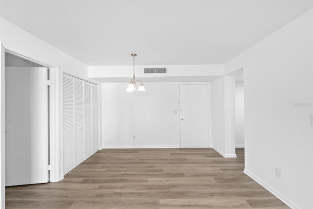 empty room with hardwood / wood-style flooring and a notable chandelier