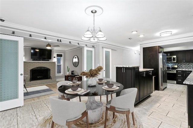 dining area featuring ceiling fan with notable chandelier, crown molding, and a brick fireplace