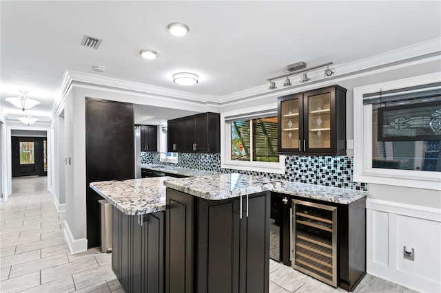 kitchen featuring light stone counters, a center island, wine cooler, dark brown cabinetry, and ornamental molding