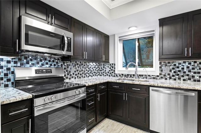 kitchen featuring sink, ornamental molding, tasteful backsplash, light stone counters, and appliances with stainless steel finishes