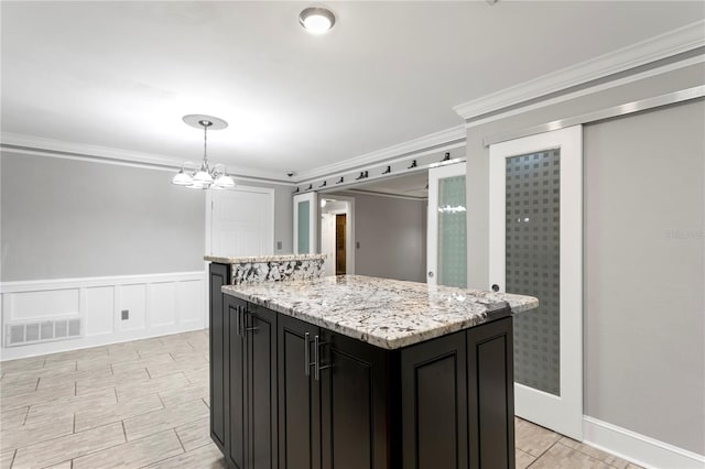 kitchen with decorative light fixtures, a kitchen island, an inviting chandelier, light stone counters, and crown molding