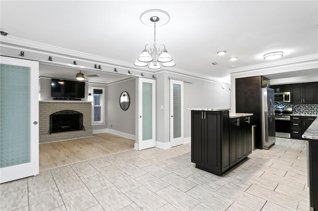 kitchen featuring appliances with stainless steel finishes, decorative backsplash, pendant lighting, ornamental molding, and a brick fireplace