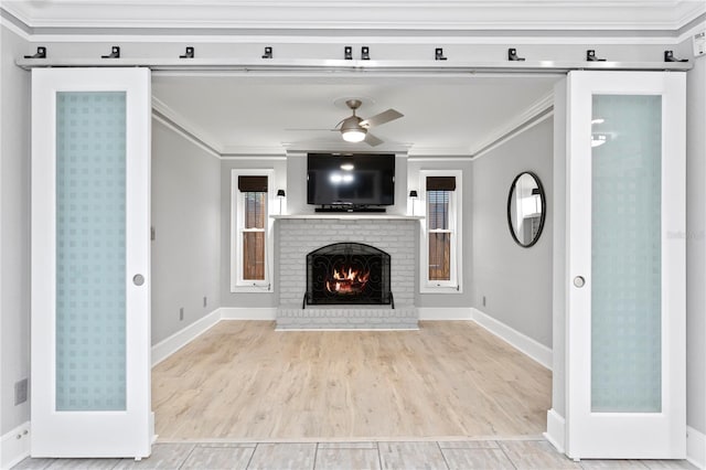 unfurnished living room featuring light hardwood / wood-style flooring, ceiling fan, crown molding, a wealth of natural light, and a brick fireplace