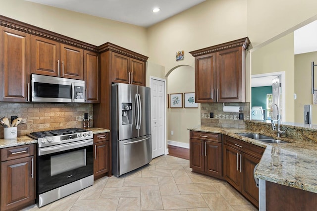 kitchen with tasteful backsplash, arched walkways, light stone counters, stainless steel appliances, and a sink