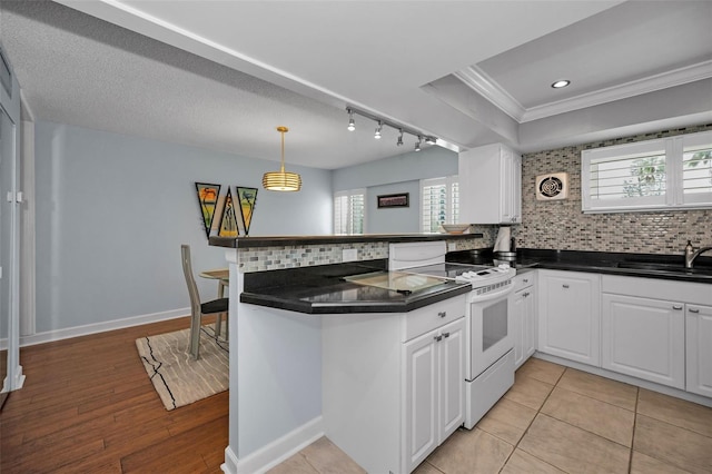 kitchen with kitchen peninsula, sink, white electric range, white cabinets, and decorative backsplash