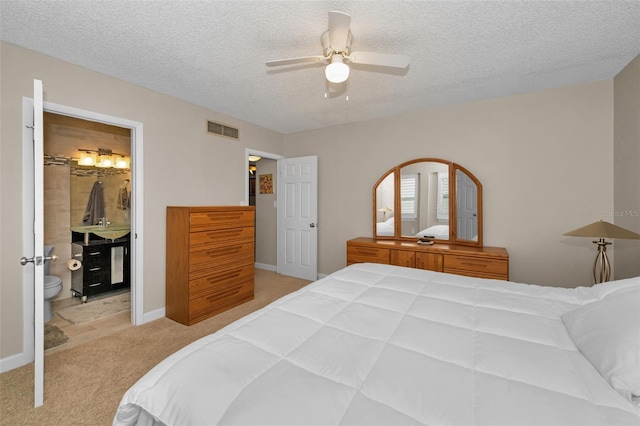 bedroom with ceiling fan, ensuite bath, a textured ceiling, and light colored carpet