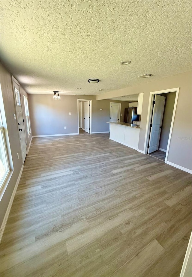 unfurnished living room with light hardwood / wood-style flooring and a textured ceiling