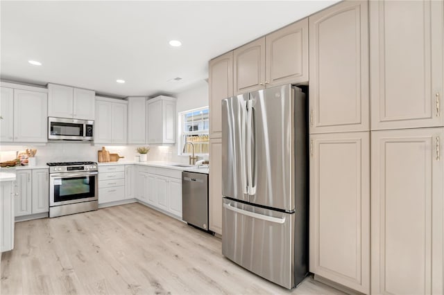 kitchen with appliances with stainless steel finishes, sink, light wood-type flooring, and backsplash