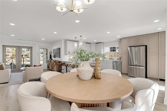 dining area featuring a healthy amount of sunlight, light hardwood / wood-style flooring, french doors, and a notable chandelier