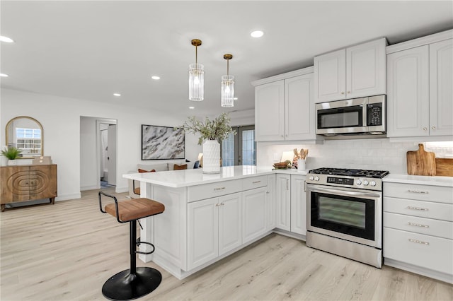 kitchen with kitchen peninsula, decorative light fixtures, tasteful backsplash, appliances with stainless steel finishes, and white cabinets