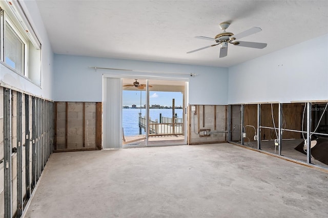 empty room featuring ceiling fan, a water view, and concrete flooring