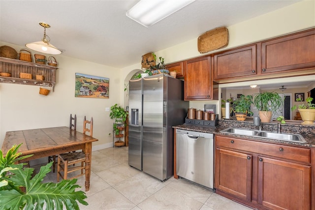 kitchen featuring arched walkways, brown cabinetry, dark countertops, stainless steel appliances, and a sink