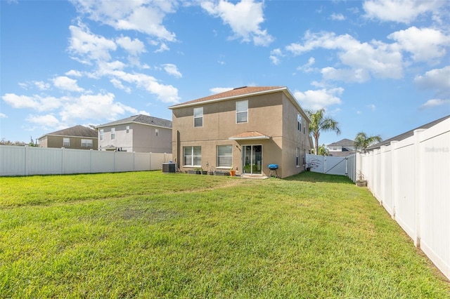 rear view of house featuring stucco siding, a lawn, a gate, central AC, and a fenced backyard