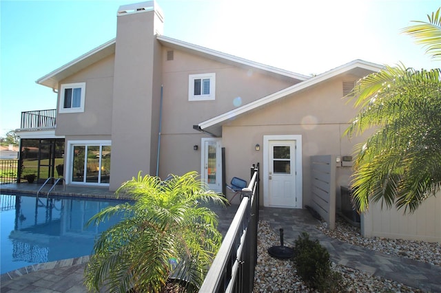 back of house with a balcony, a fenced in pool, and stucco siding