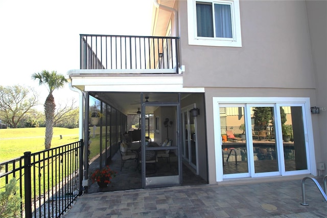 entrance to property featuring a balcony, a yard, fence, and stucco siding