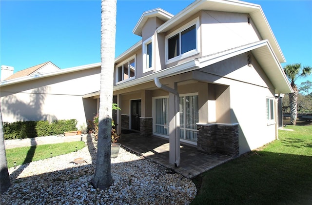 back of property with stone siding, a yard, a patio area, and stucco siding