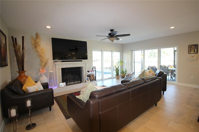 living area featuring a fireplace with raised hearth, ceiling fan, light tile patterned flooring, recessed lighting, and baseboards