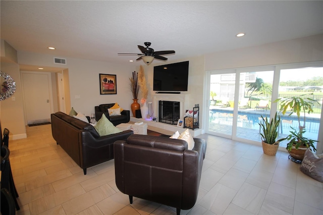 living room with visible vents, a ceiling fan, a glass covered fireplace, a textured ceiling, and recessed lighting