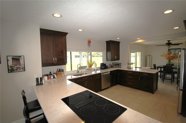 kitchen featuring dark brown cabinetry, a peninsula, stainless steel appliances, a sink, and recessed lighting