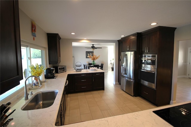 kitchen featuring light stone counters, a peninsula, stainless steel appliances, a sink, and recessed lighting