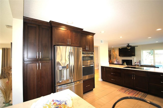 kitchen featuring visible vents, stainless steel appliances, dark brown cabinets, a fireplace, and a sink