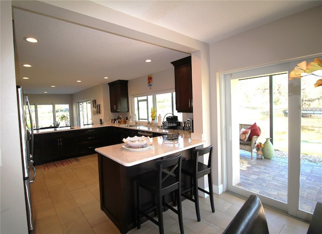 kitchen with freestanding refrigerator, a peninsula, light countertops, a sink, and recessed lighting