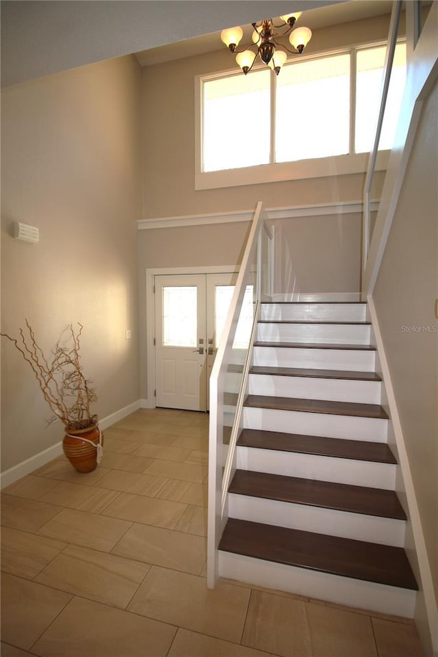 stairs with a chandelier, french doors, a towering ceiling, and a healthy amount of sunlight