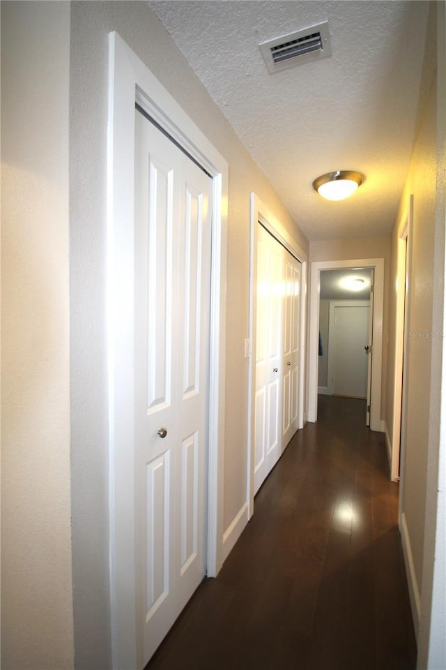 hallway featuring baseboards, visible vents, dark wood finished floors, and a textured ceiling