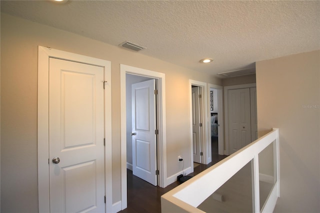 corridor featuring a textured ceiling, recessed lighting, visible vents, baseboards, and dark wood-style floors