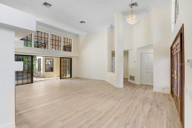 unfurnished living room featuring ornamental molding, light hardwood / wood-style flooring, a high ceiling, and an inviting chandelier