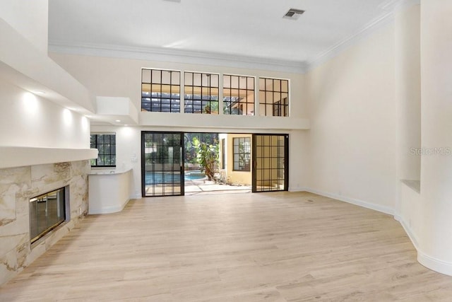 unfurnished living room with a fireplace, ornamental molding, light wood-type flooring, and a towering ceiling