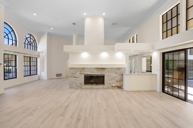 unfurnished living room with a high ceiling, a high end fireplace, crown molding, and light hardwood / wood-style floors