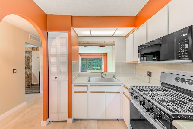 kitchen with light hardwood / wood-style flooring, gas stove, sink, white cabinetry, and decorative backsplash