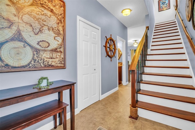 foyer with light tile patterned floors, stairs, and baseboards