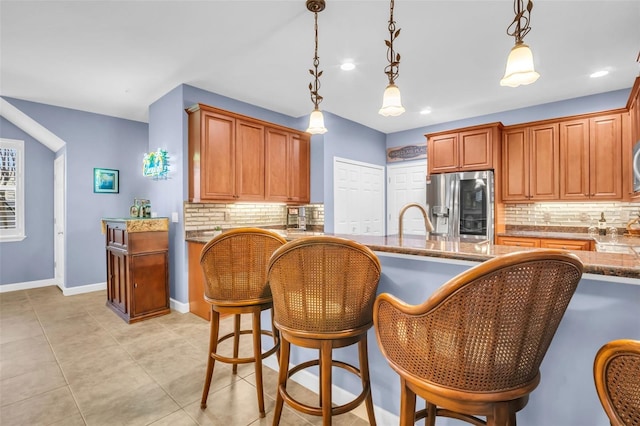 kitchen with light tile patterned floors, decorative backsplash, brown cabinetry, stainless steel fridge with ice dispenser, and decorative light fixtures