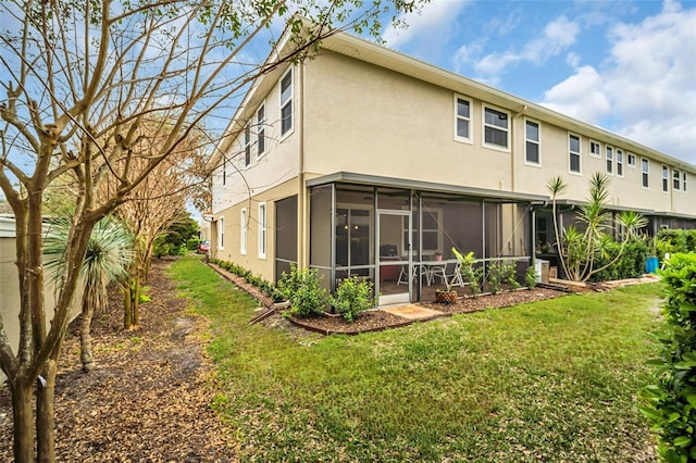 back of property with stucco siding, a sunroom, and a yard