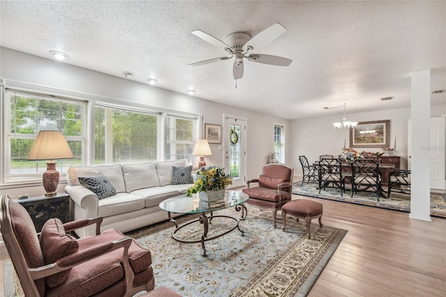 living room with ceiling fan with notable chandelier, light hardwood / wood-style flooring, and a textured ceiling