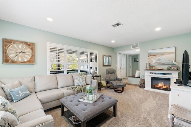 living room featuring a glass covered fireplace, visible vents, light carpet, and recessed lighting