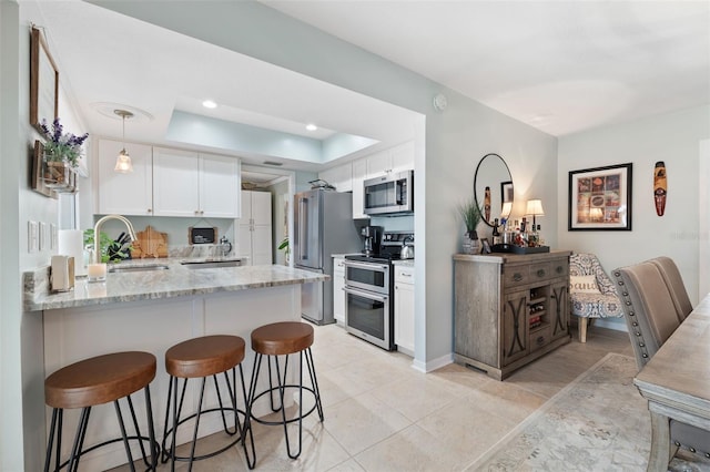 kitchen featuring a raised ceiling, a peninsula, stainless steel appliances, white cabinetry, and a sink