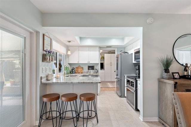 kitchen featuring stainless steel appliances, white cabinetry, a sink, light stone countertops, and a peninsula