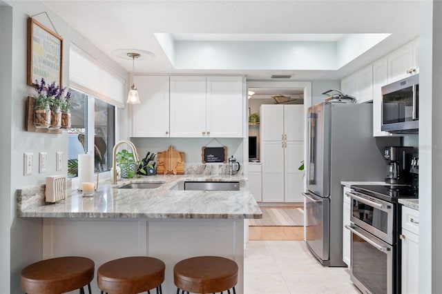 kitchen with stainless steel appliances, a peninsula, a sink, and white cabinetry