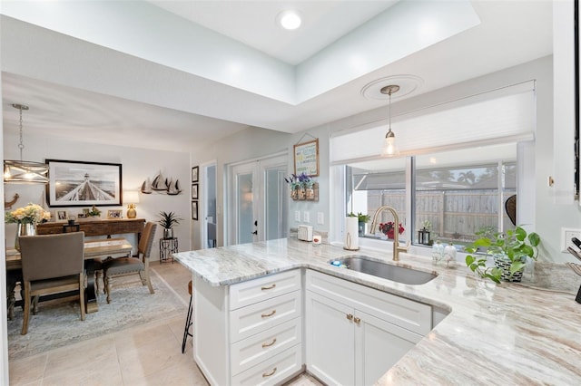 kitchen featuring a peninsula, a sink, white cabinets, hanging light fixtures, and light stone countertops