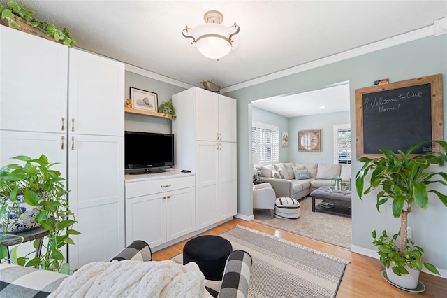 living room with crown molding, light wood-style flooring, and baseboards