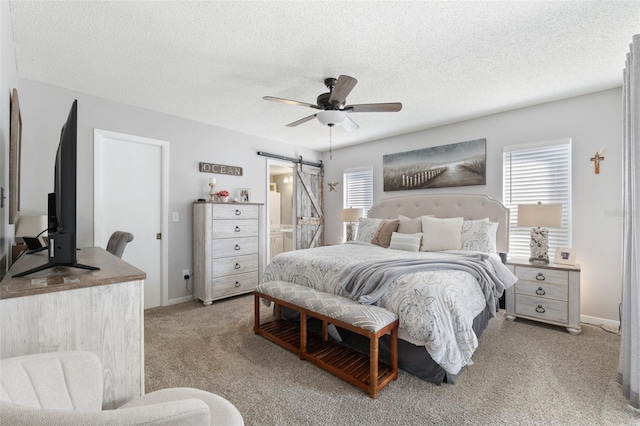 bedroom featuring a textured ceiling, ensuite bathroom, a barn door, light carpet, and a ceiling fan